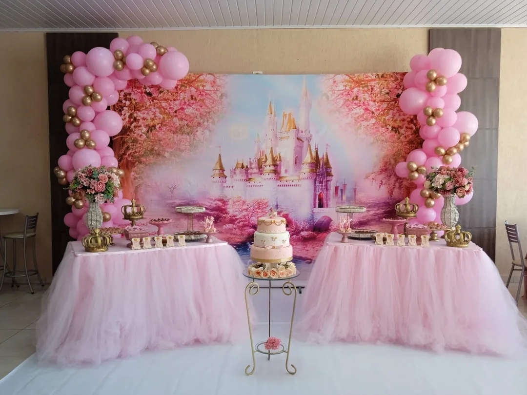Painel de castelo em tons de rosa com arco de balões rosa e dourado e mesas do bolo com saia de tule