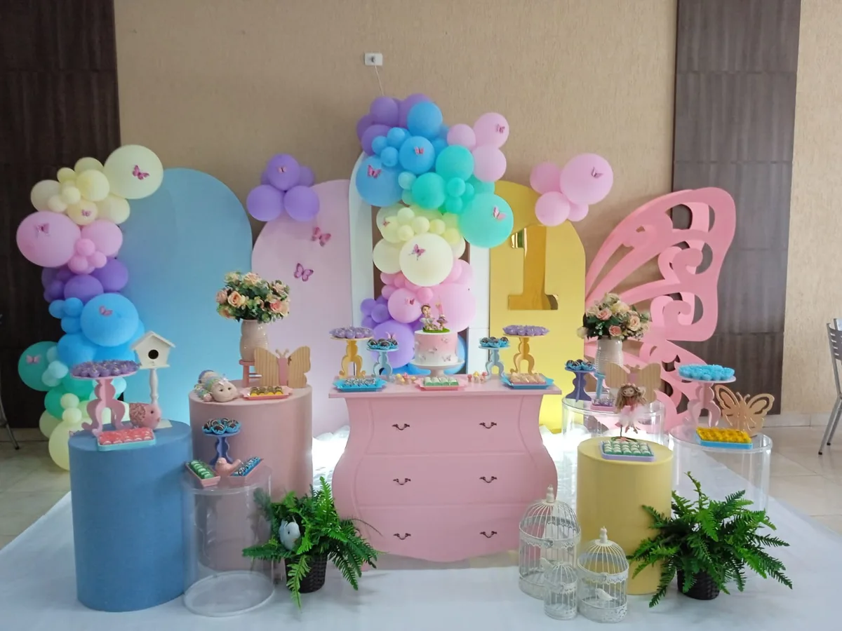 Cenário de jardim em tons pastel com borboletas, arco de balões candy color e cômoda rosa